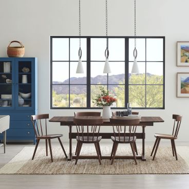 Dining room with a dark wood trestle table, spindle-back chairs, a blue glass-front cabinet, and large windows showcasing a scenic mountain view.