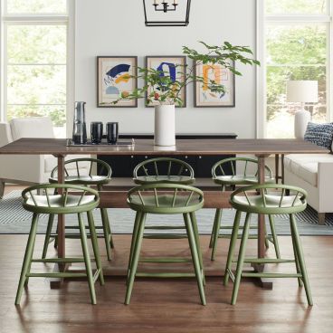 Counter height dining table with a sleek wood top, surrounded by green spindle-back chairs, set in a modern and airy dining room.