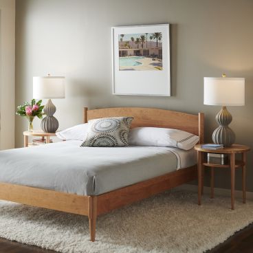 Solid cherry wood bed with a gracefully curved headboard and tapered legs, set in a modern bedroom with soft lighting