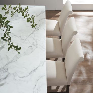 Dining chairs with upholstered backs and seats arranged alongside a sleek, marble-topped table, highlighting a blend of modern and traditional design.