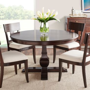 Round pedestal dining table with a dark finish, surrounded by upholstered dining chairs, creating a sophisticated and inviting dining setting.