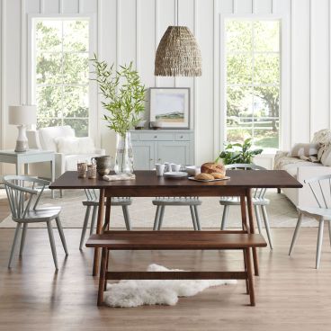 Scandinavian-style dining room with a sleek wood dining table, matching bench, and pastel spindle-back chairs, complemented by natural light and minimalist decor.