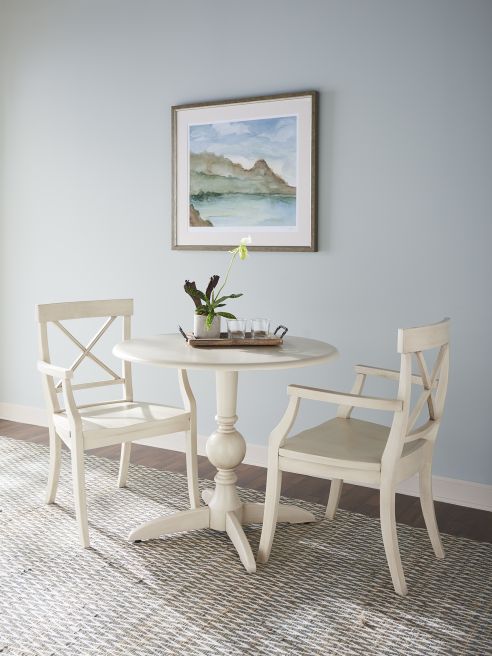 Cozy dining nook with a round pedestal table and two elegant wooden armchairs in a soft white finish