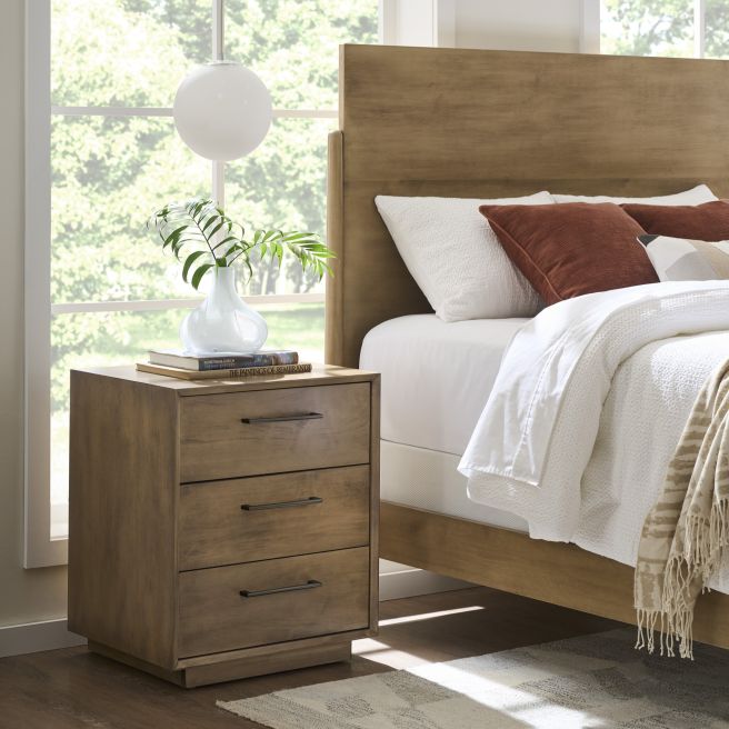 Wooden three-drawer nightstand paired with a sleek wooden bed, showcasing clean lines and functional design in a contemporary bedroom setting.
