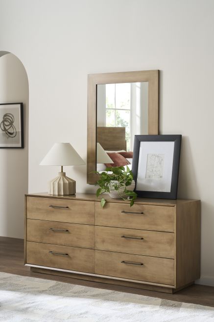 A wooden six-drawer dresser paired with a rectangular mirror, featuring sleek handles and a minimalist design, complemented by decorative accents.