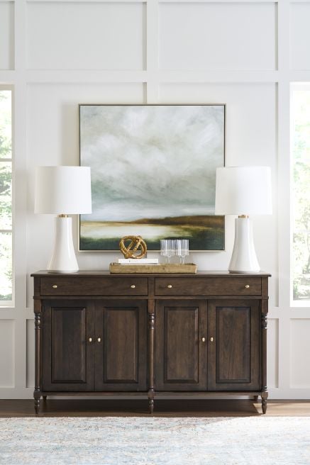 A dark-stained wooden buffet with framed art and modern decor is styled in a bright dining room. A perfect example of handcrafted sustainable furniture