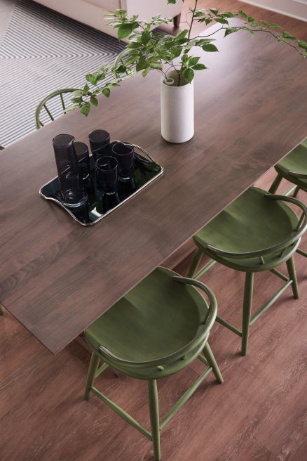 Close-up of a solid wood counter height table paired with green spindle-back chairs, showcasing smooth craftsmanship and modern design.