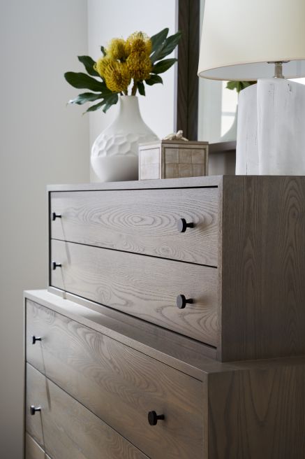 Close-up of a modern wooden dresser with sleek black knobs, styled with a vase of yellow flowers.