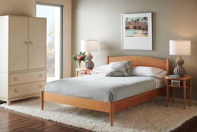 Minimalist cherry wood bed frame with a natural finish, featuring a gently arched headboard and handcrafted joinery