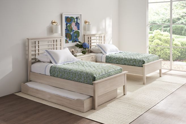 Two twin beds and a trundle bed with light wood headboards and green bedding, positioned in a well-lit room with large windows and garden views.