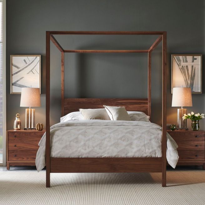 Wood platform bed with a canopy frame, flanked by matching nightstands and warm lighting in a modern, minimalist bedroom.