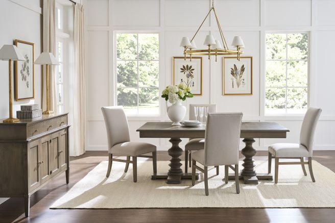 Wooden dining table with turned pedestal base, paired with neutral upholstered chairs.