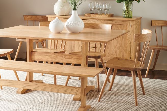Farmhouse trestle table with matching wooden chairs and bench, set in a bright dining room with natural decor and soft lighting.