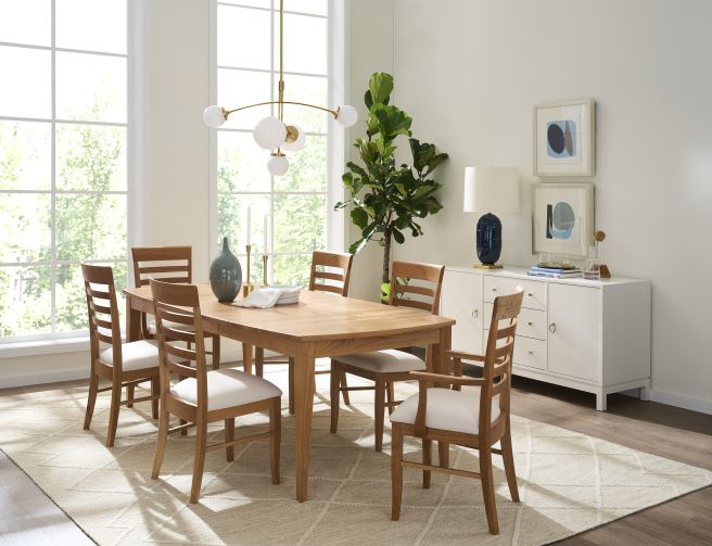 Natural wood dining table with matching chairs, styled with neutral decor and a white sideboard in a sunlit room.