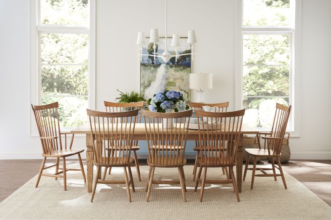 Dining room with a solid wood table and chairs featuring a natural finish, complemented by large windows and a simple chandelier