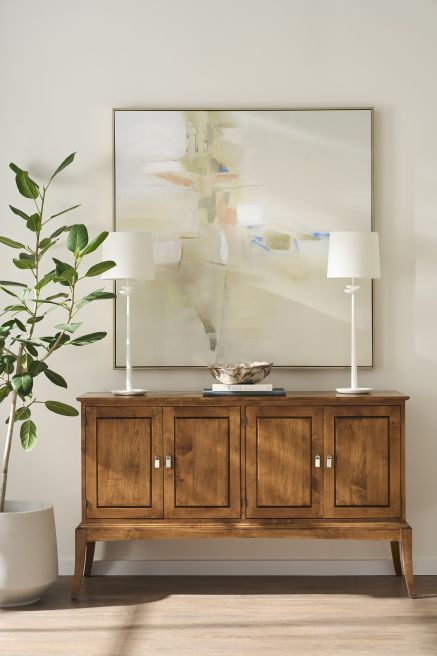 Solid wood console table with natural finish framed by contemporary artwork and elegant white lamps.