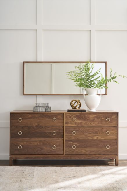 Walnut wood dresser with gold hardware, styled with decorative accents and a modern mirror above.